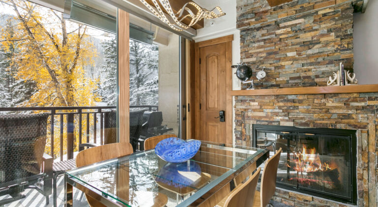 dining area of antlers at vail condo 106 with cozy gas fireplace and large windows out to creek