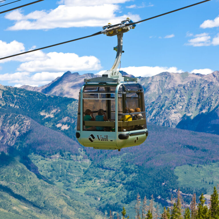 Gondola taking guests up to the top of Vail Mountain in the summer with gore range as the backdrop