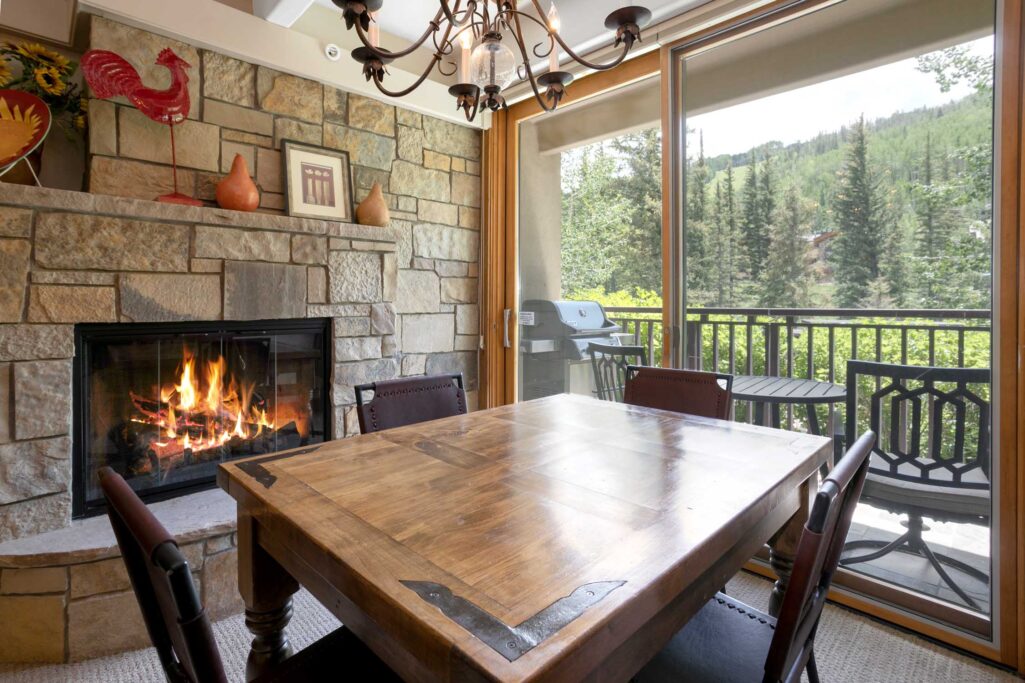 dining area of Antlers at Vail unit 111 with windows to the creek outside and cozy gas fireplace