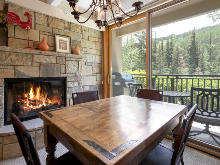 dining area of Antlers at Vail unit 111 with windows to the creek outside and cozy gas fireplace