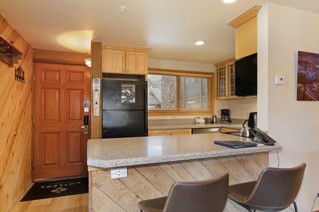 Entry and kitchen bar area of Antlers at Vail condo 502 with granite breakfast bar, bar stools, black refrigerator, and ski storage near the front door