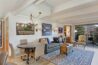 Open-concept living and dining area in Antlers at Vail condo 502 with gray sofa, blue patterned area rug, round dining table, exposed beam ceiling, and balcony access