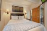 Primary bedroom in Antlers at Vail condo 502 featuring a queen bed with wood headboard, flanking sconce lights, aspen tree artwork, and private balcony access