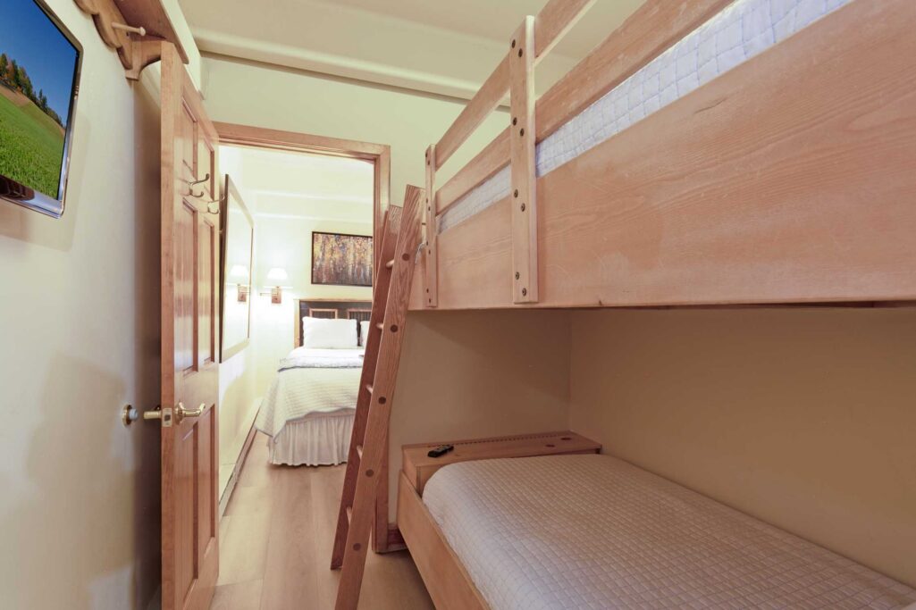 Bunk room in Antlers at Vail condo 502 with twin-over-twin wood bunk beds, wall-mounted TV, and open doorway to adjacent bedroom