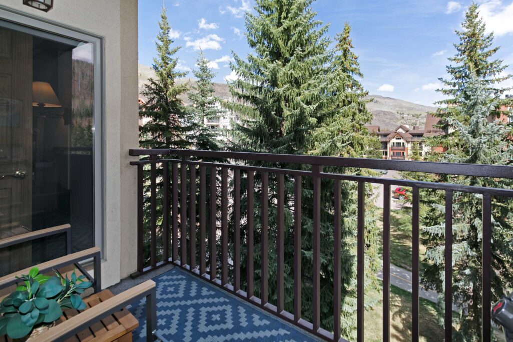 Private balcony of Antlers at Vail condo 502 with outdoor seating overlooking tall evergreen trees and mountain views in summer