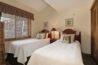 Antlers at Vail condo 515 twin bedroom with two beds with cherry wood headboards, dog-themed accent pillows, shared nightstand with red lamp, and wood-framed window with plaid valance