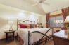 Antlers at Vail condo 515 primary bedroom with ornate iron bed frame, red and floral accent pillows, plaid curtains, ceiling fan, round wood nightstand, and red leather chair