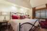 Antlers at Vail condo 515 primary bedroom with ornate iron bed frame, red and floral decorative pillows, plaid curtains, vaulted ceiling with recessed lighting, and red leather accent chair