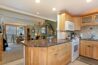 Antlers at Vail condo 607 kitchen with granite island, white range and microwave, warm wood cabinetry, tile backsplash, and open view into the living area with antler chandelier, sage green accent wall, vintage sled décor, and balcony beyond