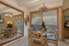 Antlers at Vail condo 607 dining area with round glass-top table, rustic log chairs, antler chandelier, large wall mirror, decorative snowshoes, and sliding glass door to balcony with pine tree and mountain views