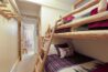 Antlers at Vail condo 607 bunk bedroom with rustic log twin-over-twin bunk beds, red plaid and pine tree bedding, log coat rack, hallway leading to bathroom with shower curtain visible in background