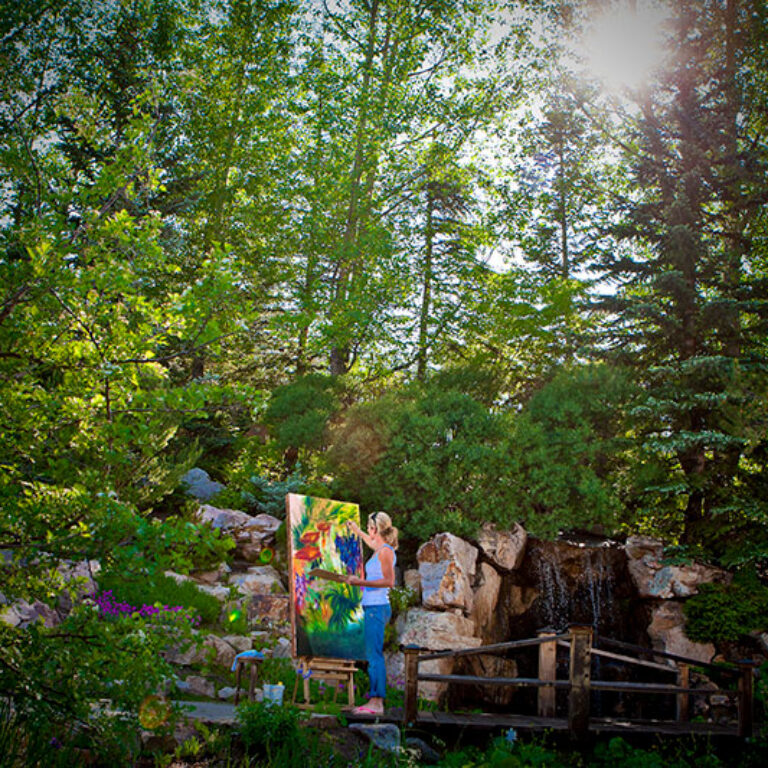 Painter creating artwork in a lush garden setting with waterfall features at Betty Ford Alpine Gardens in Vail, Colorado.