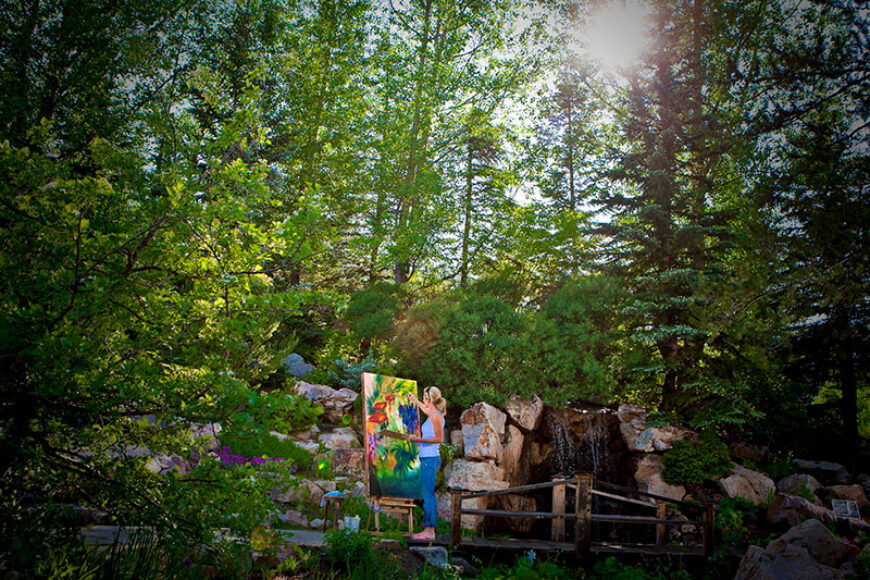 Painter creating artwork in a lush garden setting with waterfall features at Betty Ford Alpine Gardens in Vail, Colorado.