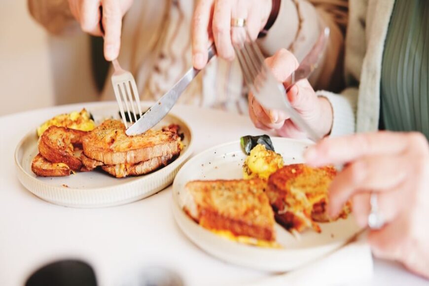 Breakfast plate with French toast, eggs and potatoes being shared at a table.